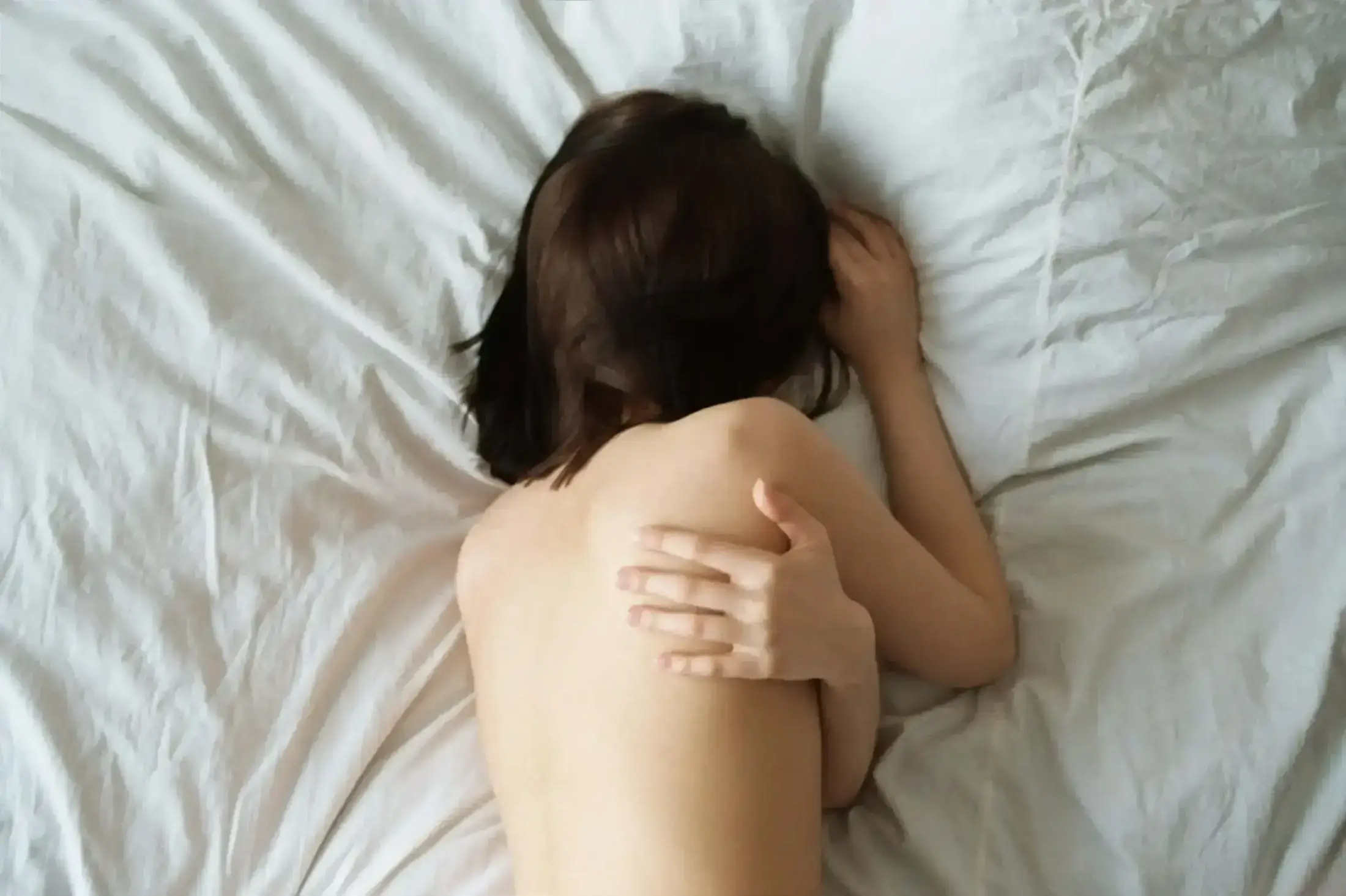 Back view of a woman lying on white bed sheets.