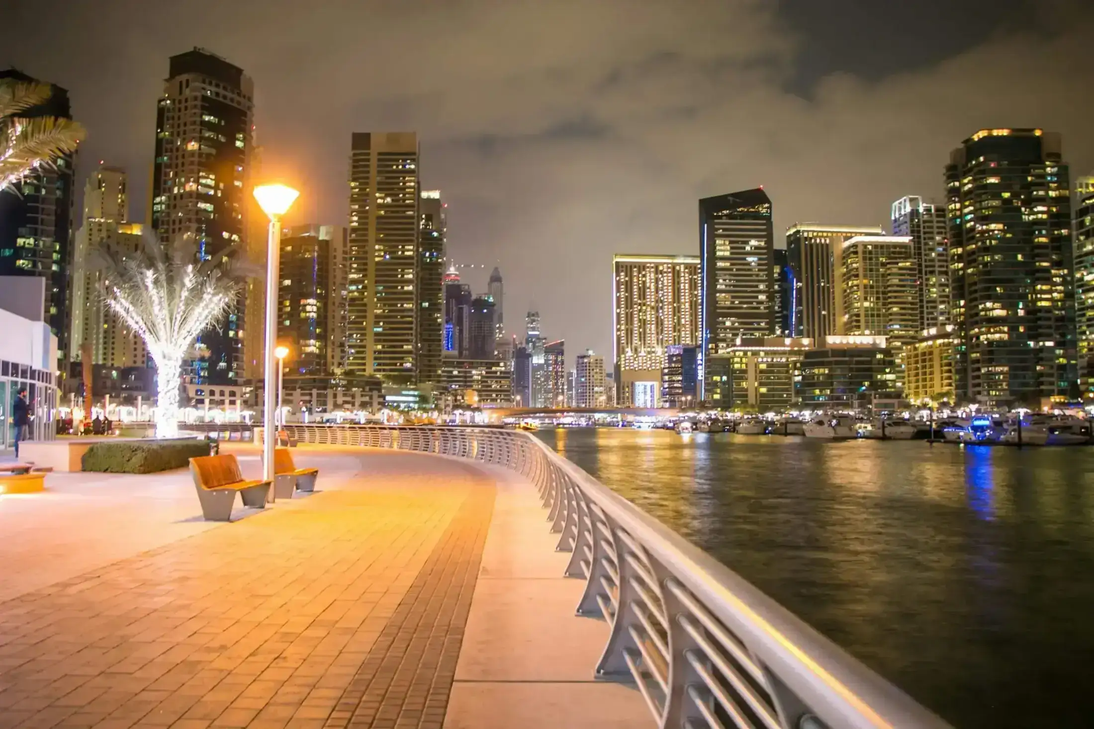 Night view of Dubai Marina promenade with illuminated skyscrapers.