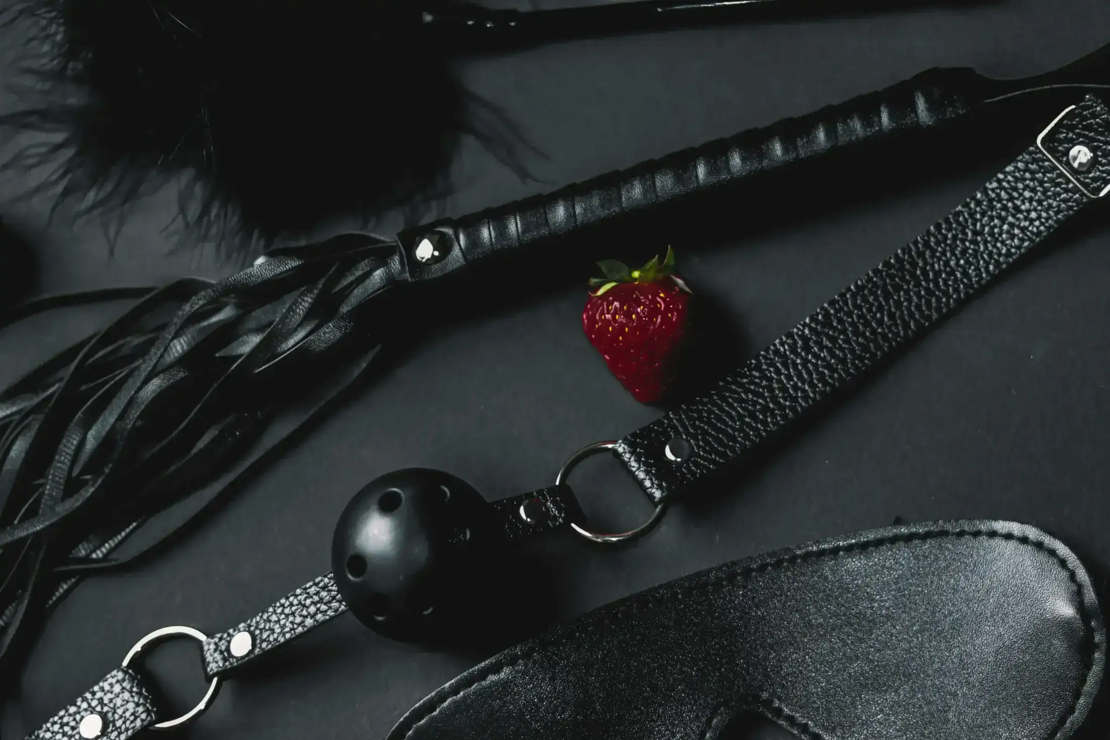Black leather BDSM accessories and a single red strawberry.