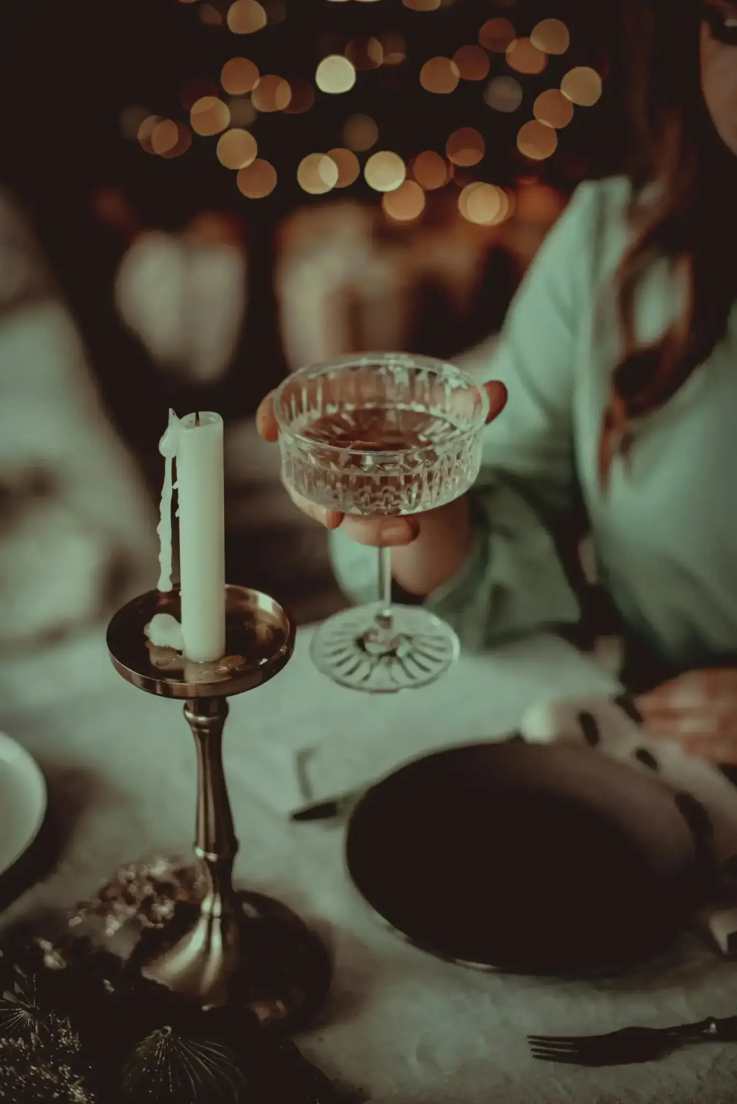 A hand holding a crystal cocktail glass near a candle.
