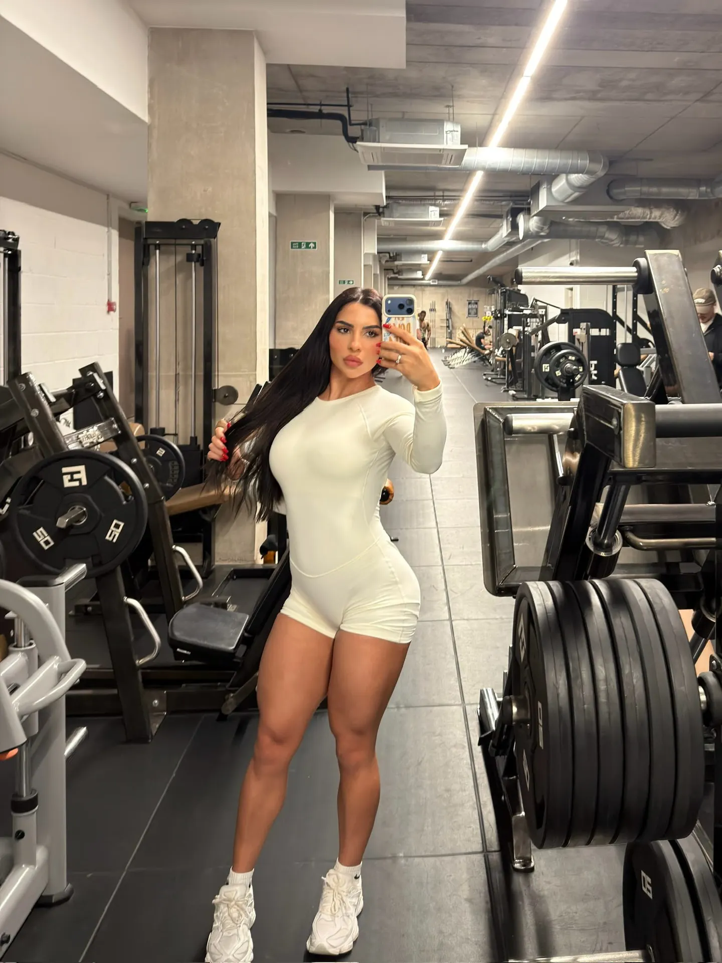 Woman in white gym wear taking a mirror selfie.