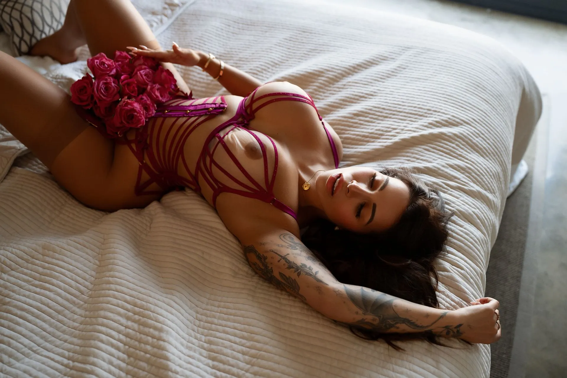 Woman in magenta lingerie lying on a bed with roses.