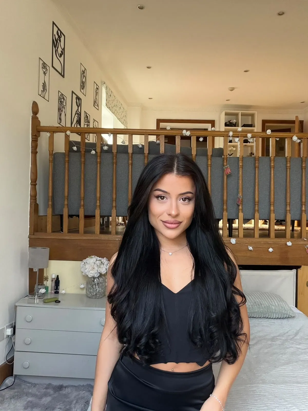 Woman with long black hair posing in a bedroom.